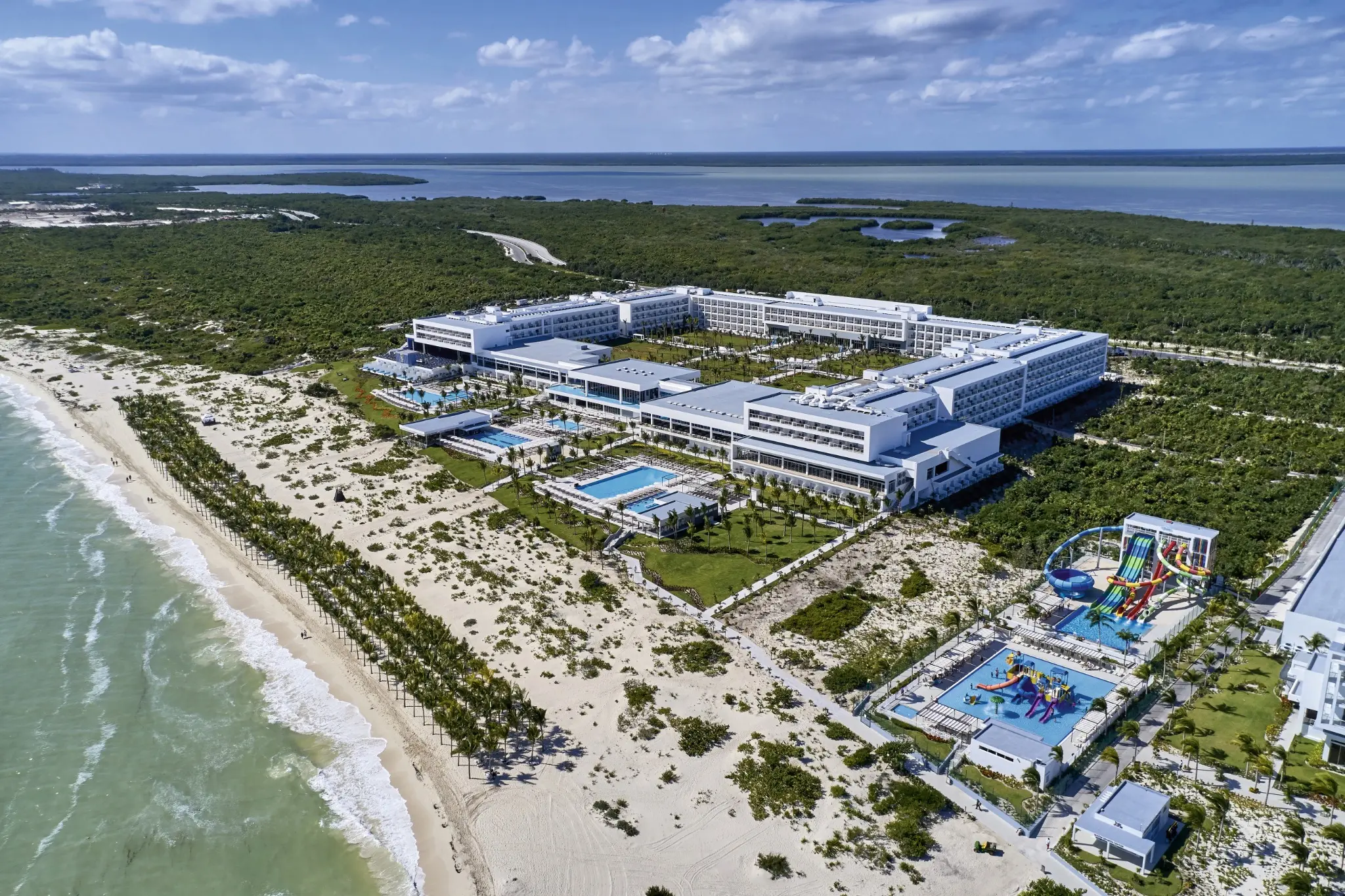 Aerial view of RIU Palace Costa Mujeres, its beachfront, pools, tropical grounds, and nearby waterpark