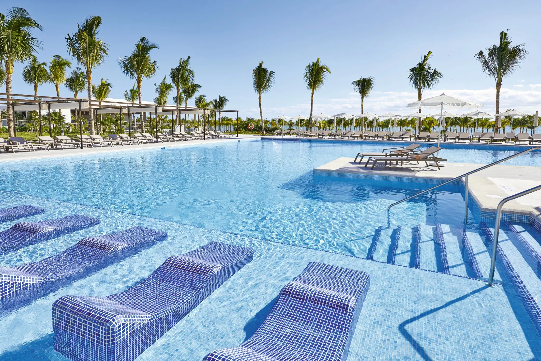 Large blue swimming pool with submerged loungers at RIU Palace Costa Mujeres
