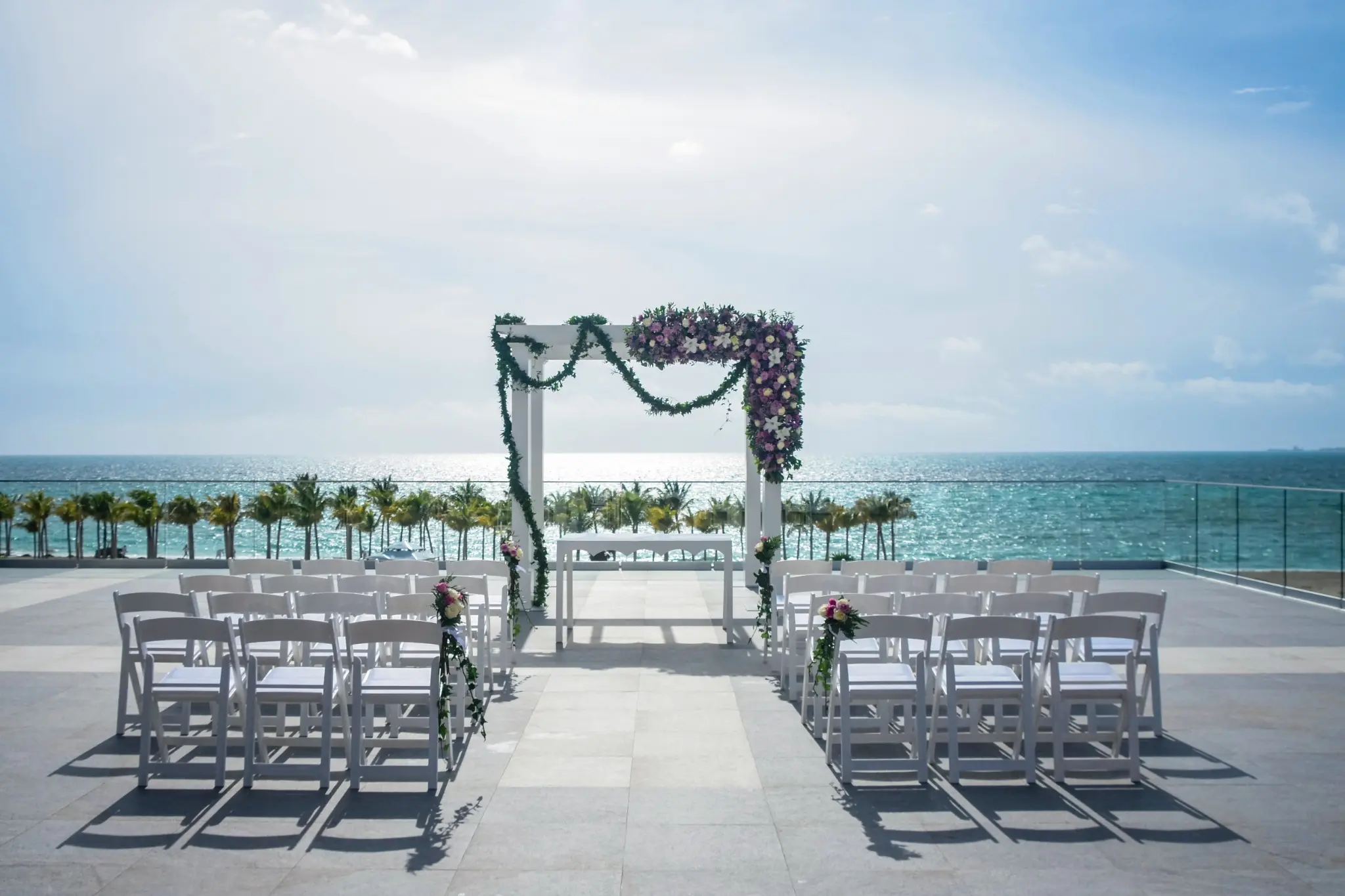 Ocean-view wedding terrace prepared with white chairs and a floral ceremony arch at RIU Palace Costa Mujeres
